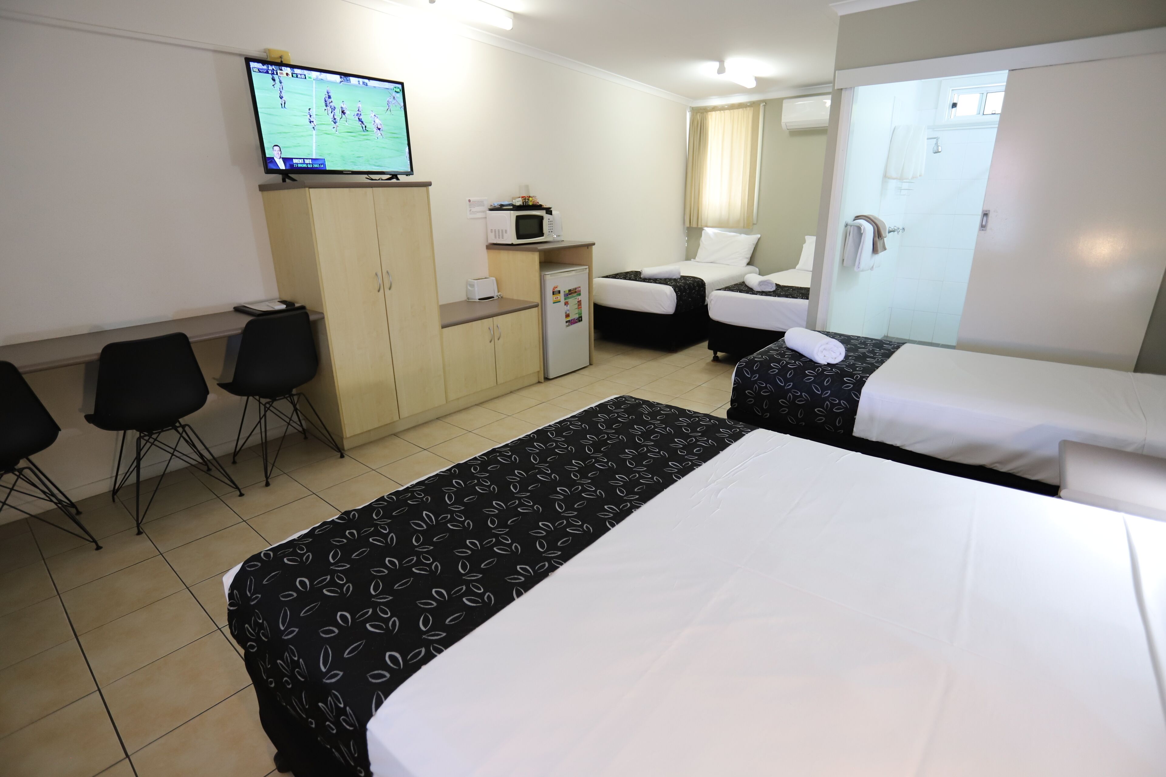 A hotel room with two beds, a TV, a microwave, a refrigerator, a desk, and a bathroom.