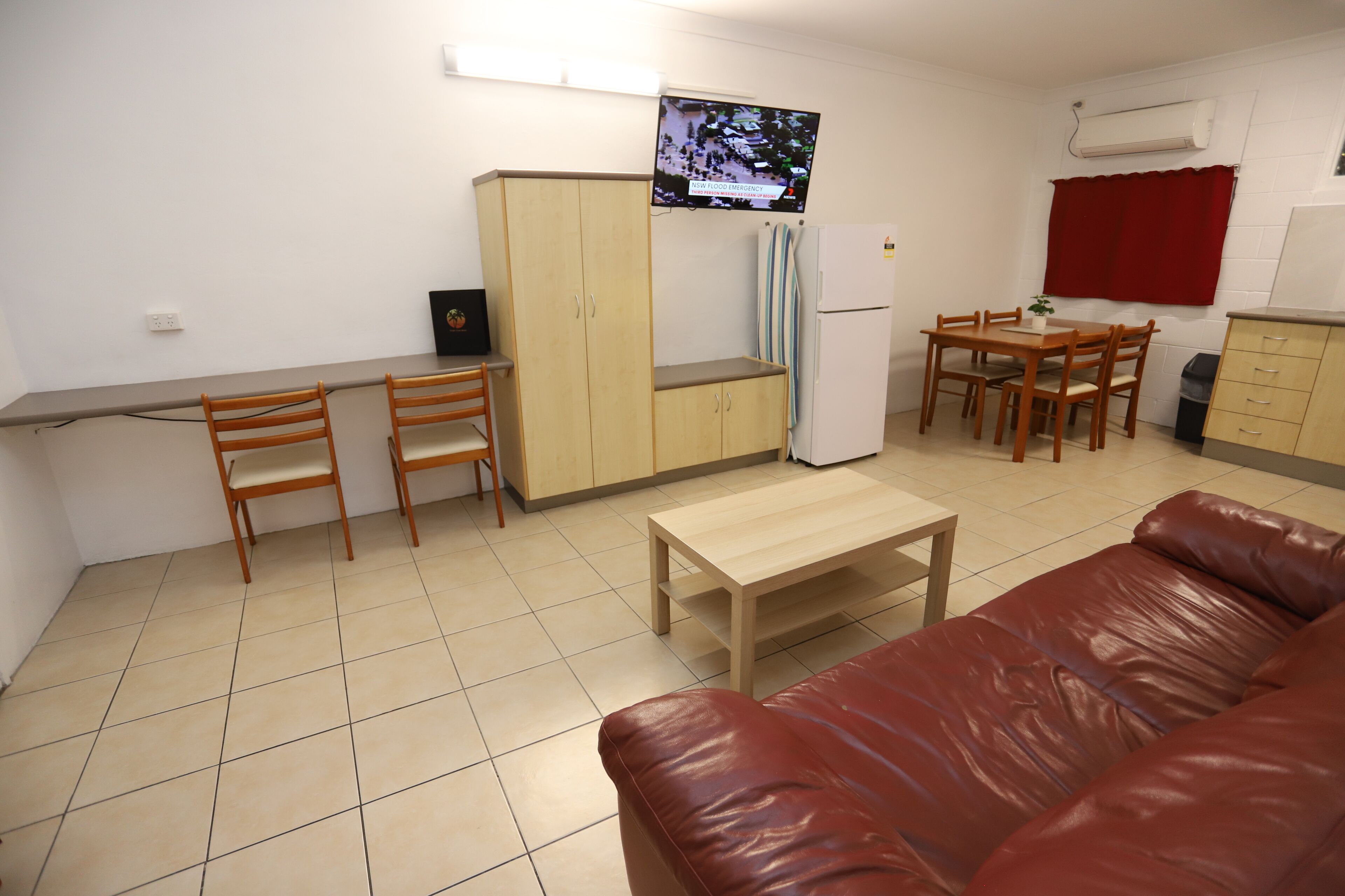 A compact living space with a kitchenette, a dining area, a sofa, and a TV mounted on the wall.