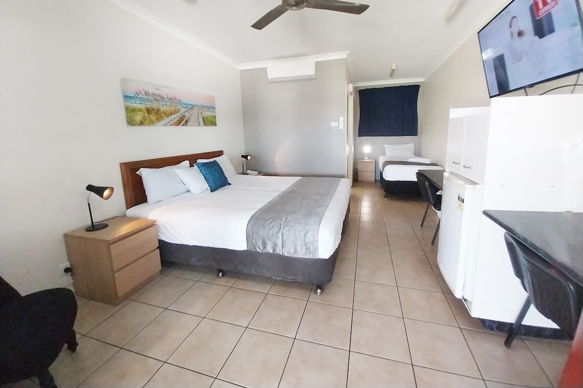 Une chambre d’hôtel avec un lit, un bureau, une chaise, une télévision, un ventilateur de plafond et un tableau au mur.