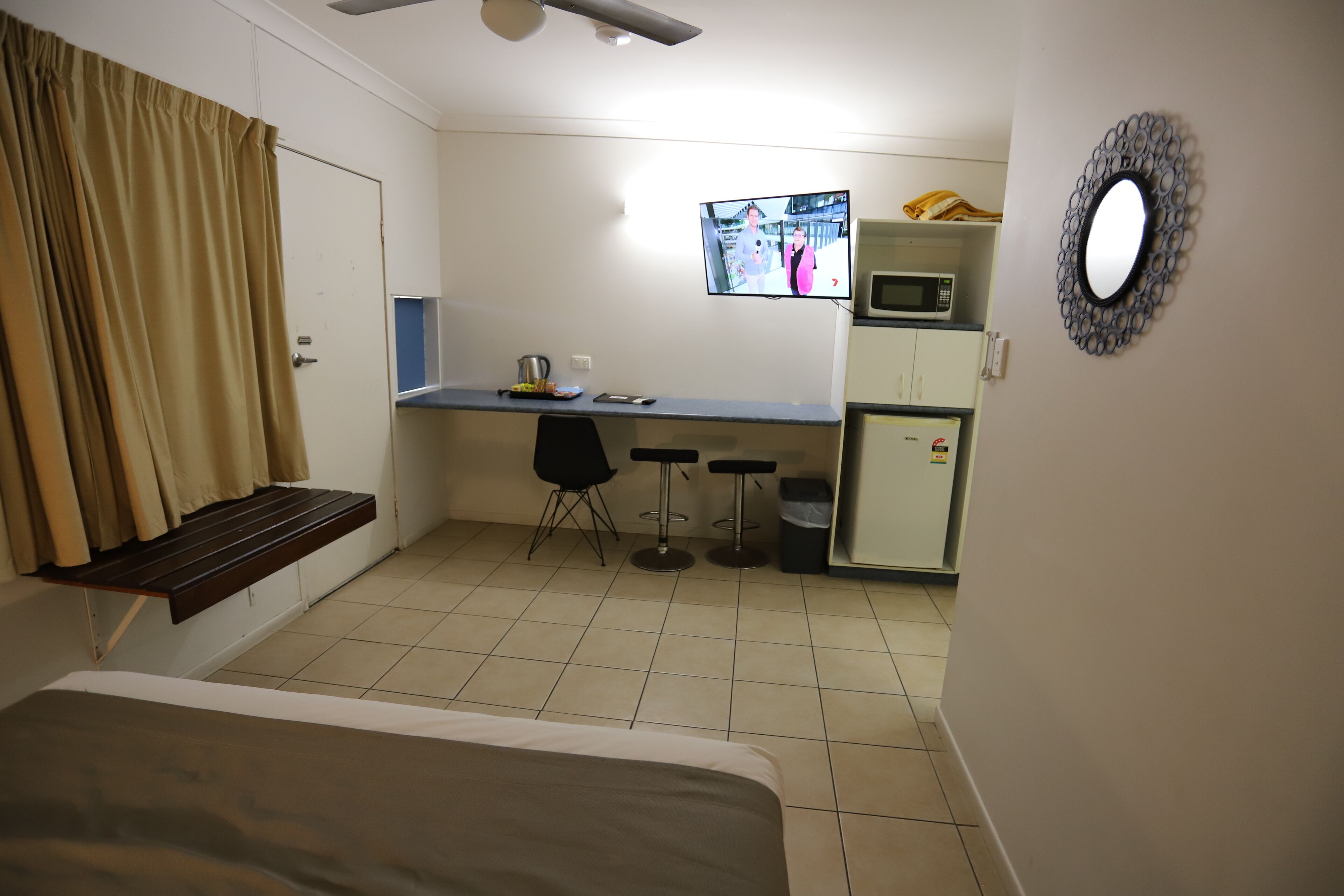 Une chambre d’hôtel compacte comprenant un lit, un bureau, un four à micro-ondes, un petit réfrigérateur, une télévision et un miroir.