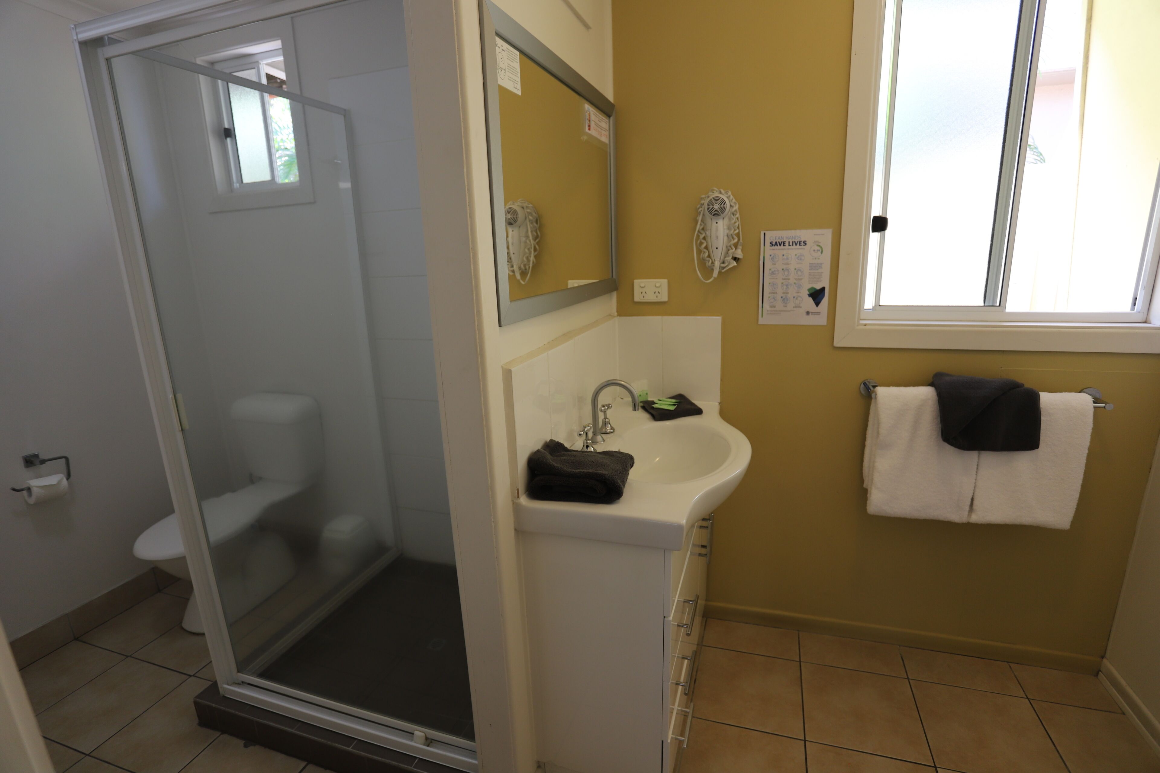 A bathroom with a glass shower enclosure, a white sink, a mirror, and a window.