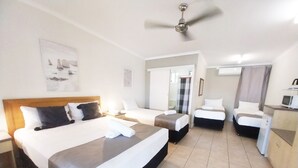A hotel room with a large bed, two smaller beds, a desk with a computer, and a ceiling fan. - Tropic Coast Motel (West Mackay)