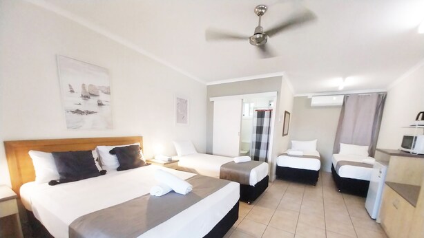 A hotel room with a large bed, two smaller beds, a desk with a computer, and a ceiling fan. - Tropic Coast Motel (West Mackay)