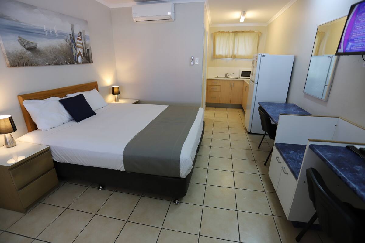 Une chambre d’hôtel équipée d’un lit, de lampes de chevet, d’un bureau, d’une chaise, d’un réfrigérateur et d’un coin cuisine.