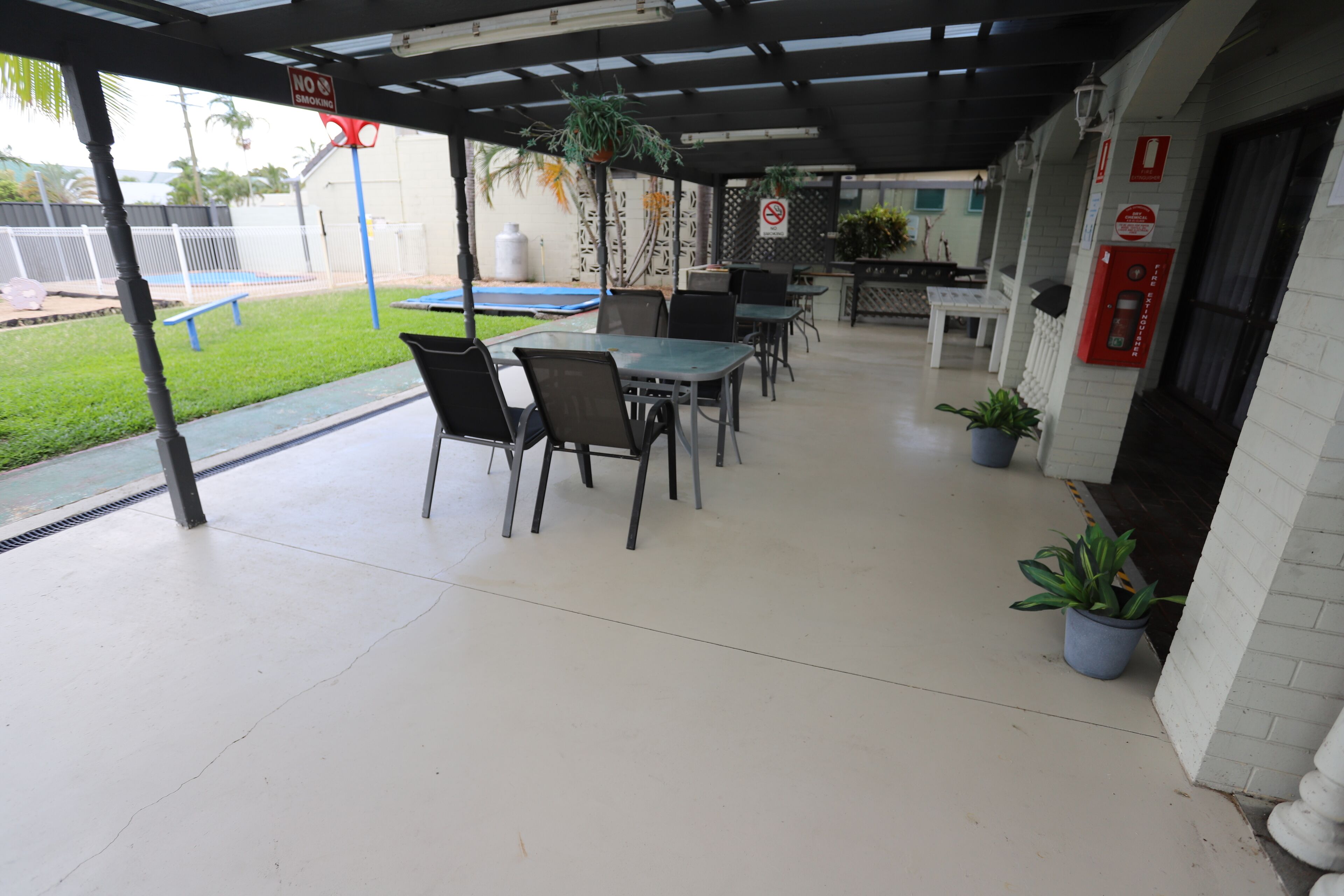 An outdoor patio area with tables and chairs, potted plants, and a no-smoking sign.
