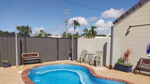 A backyard with a swimming pool, a wooden bench, and a small table with chairs. - Tropic Coast Motel (West Mackay)