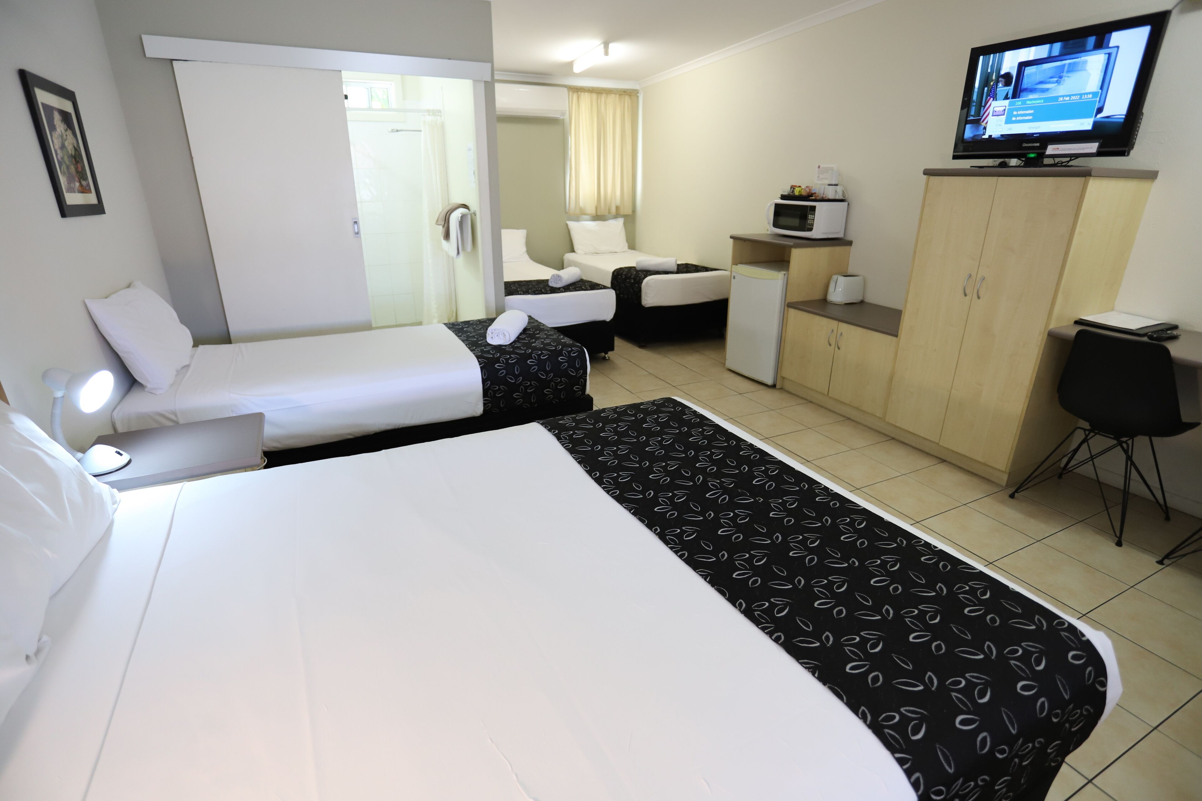 A hotel room with two beds, a desk, a TV, and a minibar.