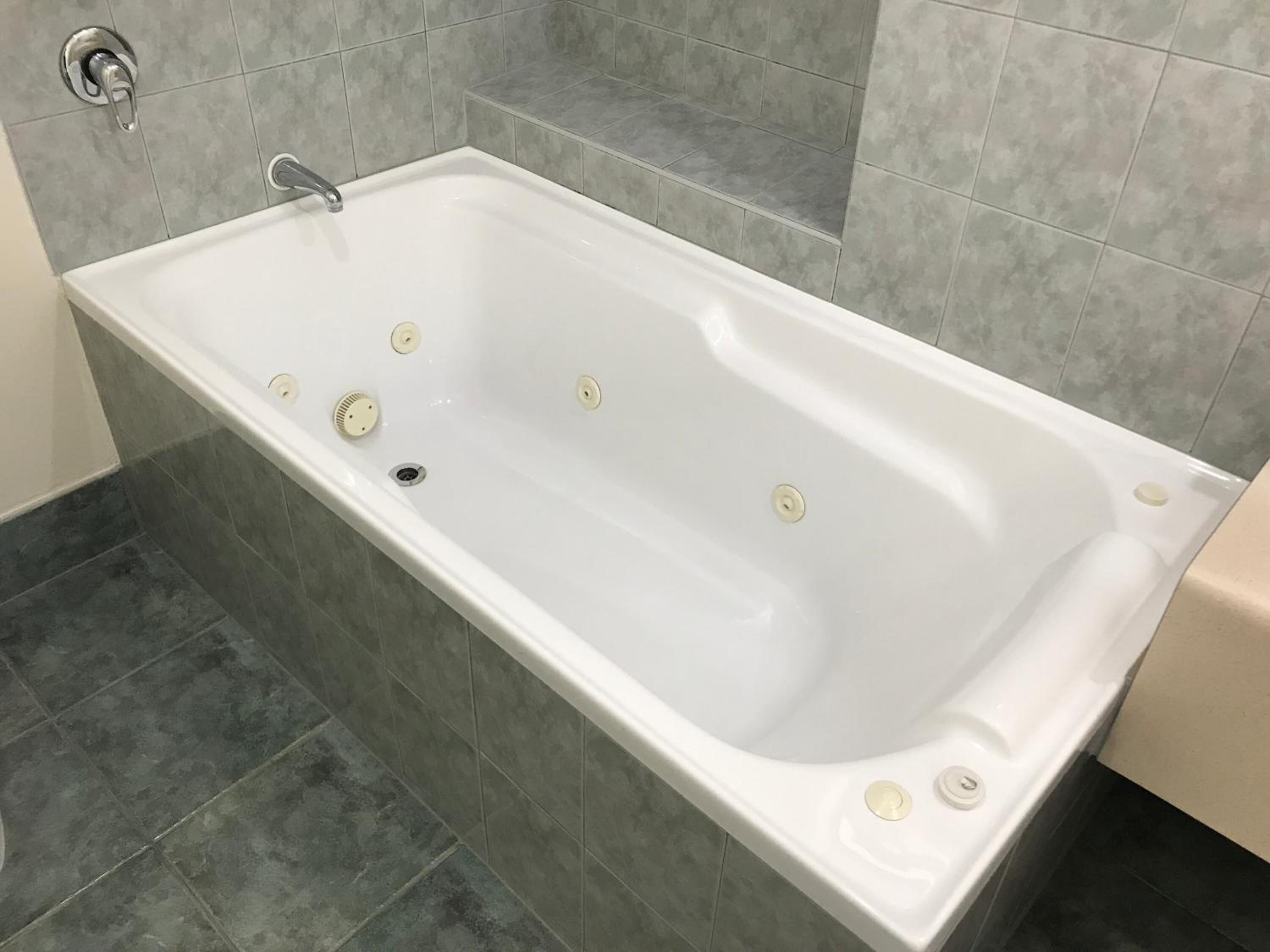 Un baño moderno con una bañera rectangular, paredes de azulejos grises y piso oscuro.