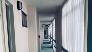 Un corridoio con tappeto blu, pareti bianche, una telecamera di sicurezza nera e una porta bianca.