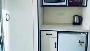 Un angolo cottura compatto con forno a microonde, un piccolo frigorifero e uno scaffale con stoviglie.