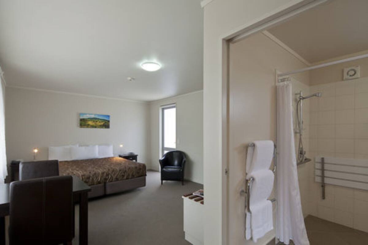 A hotel room with a bed, a chair, a shower, and a painting on the wall.