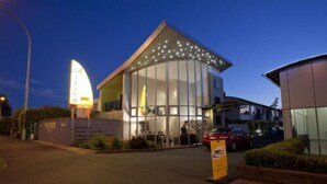 A modern building with a curved glass facade, a prominent sign with 'TRIUM' and 'VACANCY' visible, and a parking area with cars.
