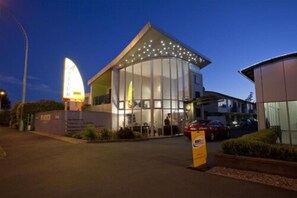 A modern building with a curved glass facade, a prominent sign with 'TRIUM' and 'VACANCY' visible, and a parking area with cars.