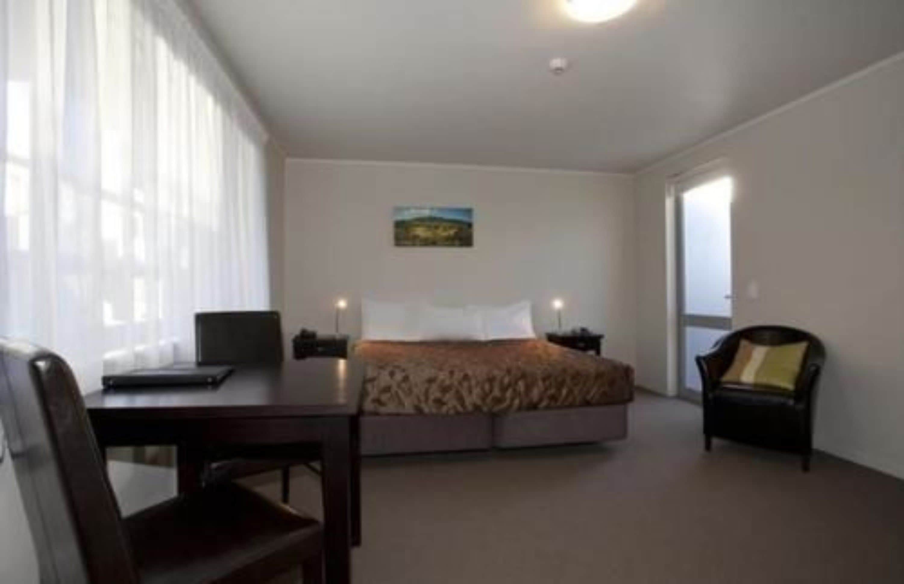 Un dormitorio con una cama, un escritorio, una silla y una ventana con cortinas.