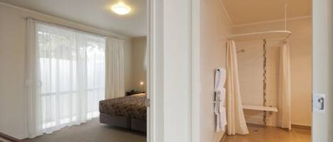 Una habitación de hotel con una cama, una mesita de noche y un ventanal con cortinas.