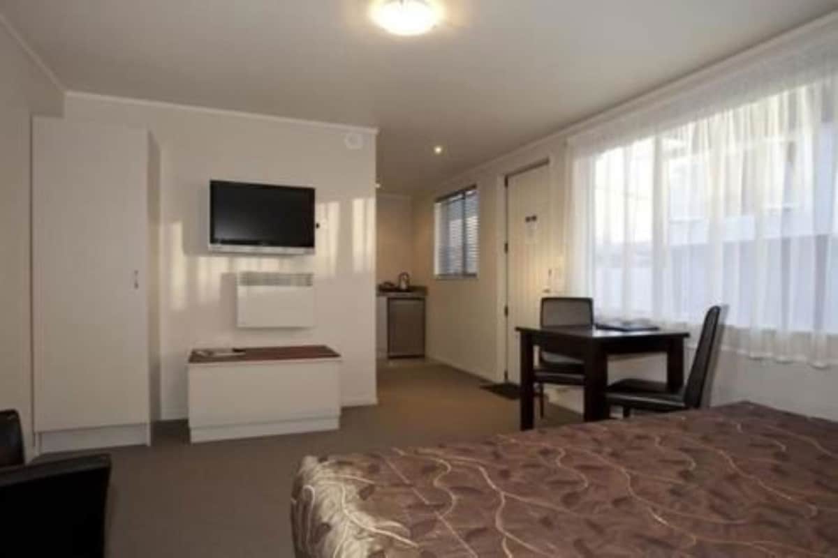 Ein Hotelzimmer mit Bett, Schreibtisch mit Stuhl, Wandfernseher und einem Vorhangfenster.