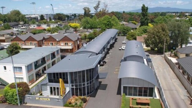 A modern building with a curved glass facade, a parking lot, and a small garden area.