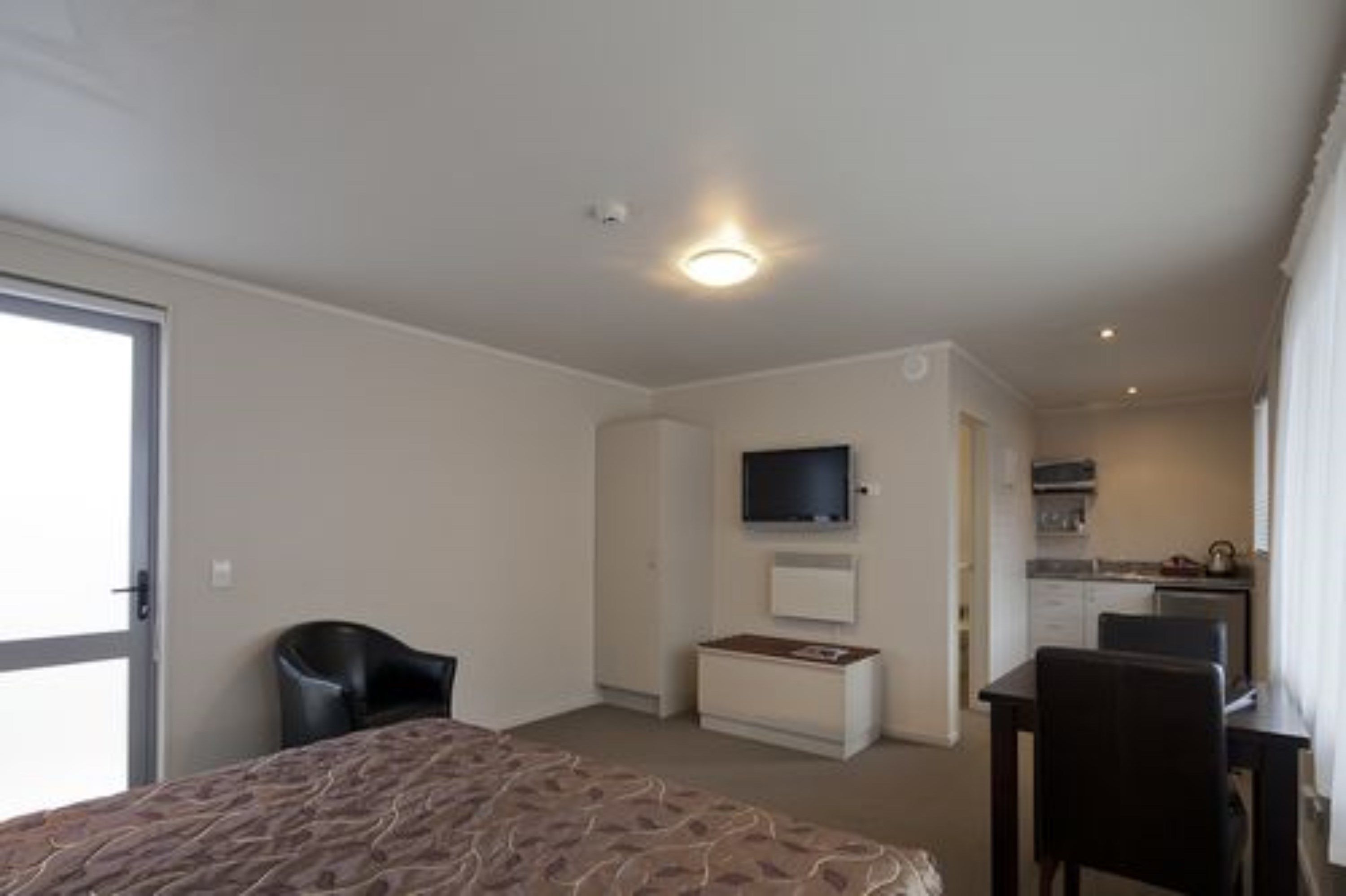 A hotel room with a bed, a desk, a chair, a television, and a kitchenette.