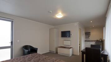 Quarto de hotel com cama, escrivaninha, cadeira, televisão e cozinha compacta.