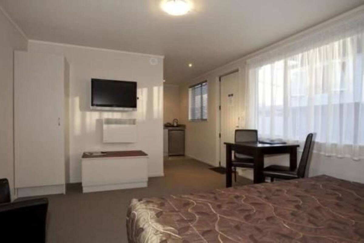 A hotel room with a bed, a desk with a chair, a television mounted on the wall, and a window with curtains.
