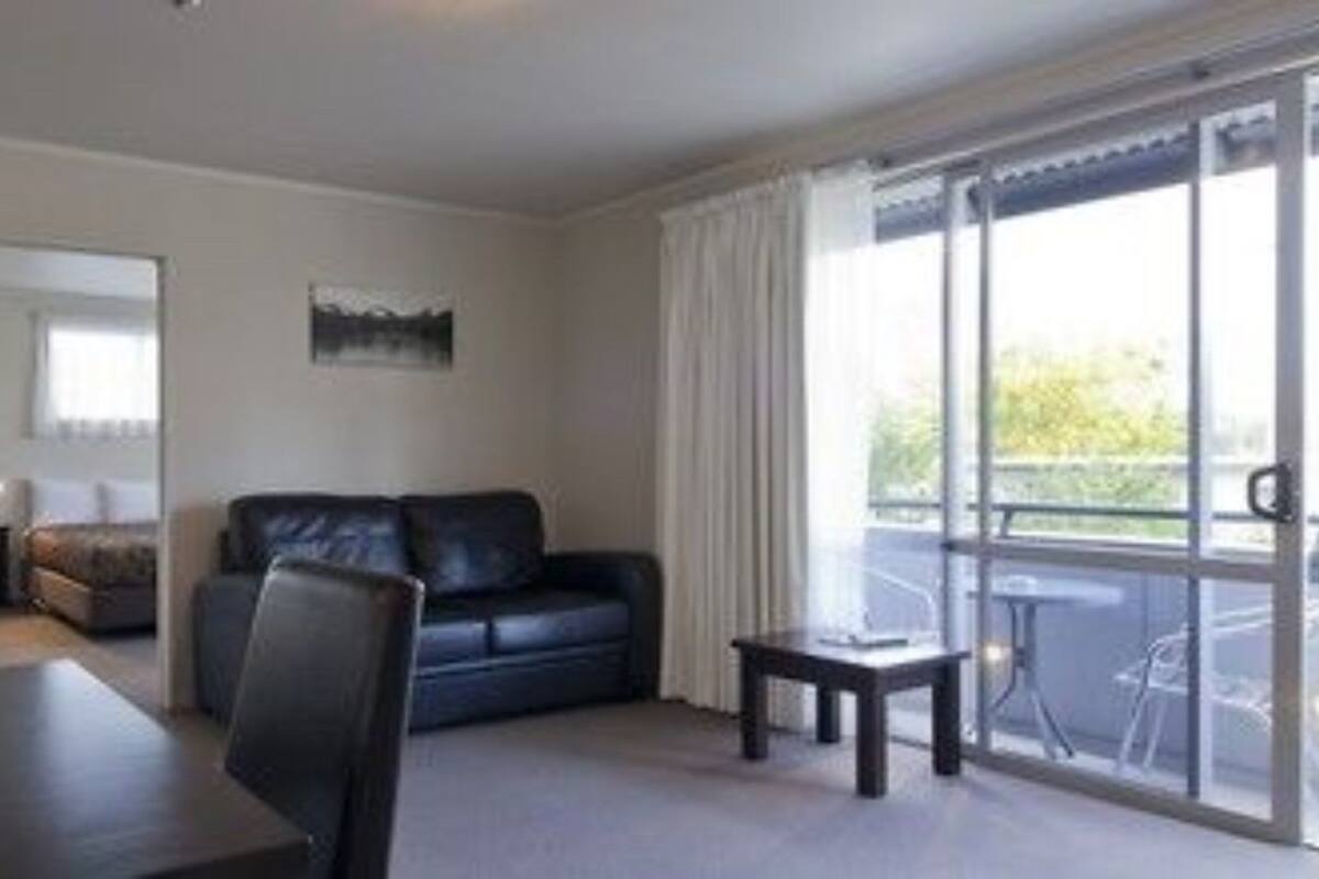 A modern living room with a black leather sofa, a dining table with chairs, and a balcony with a view.