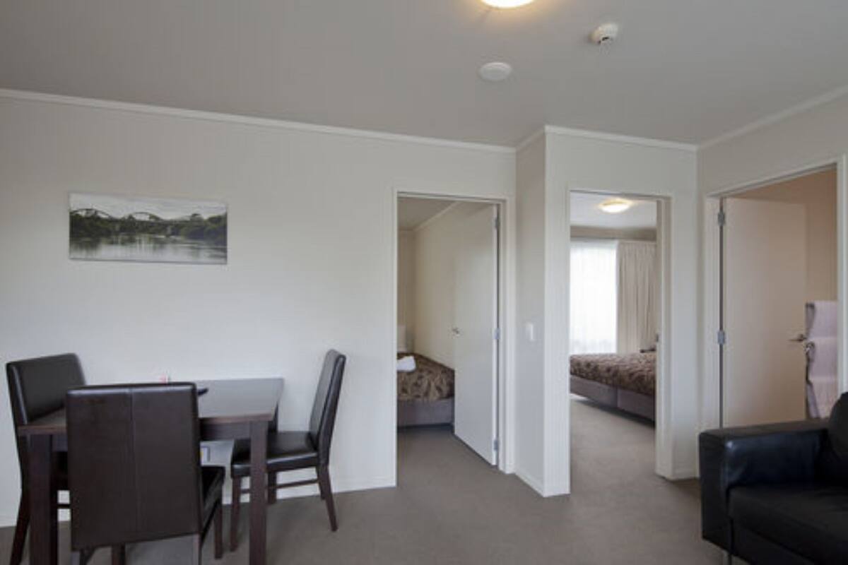 A room with a dining table and chairs, a bed with a headboard, and a doorway leading to another room.