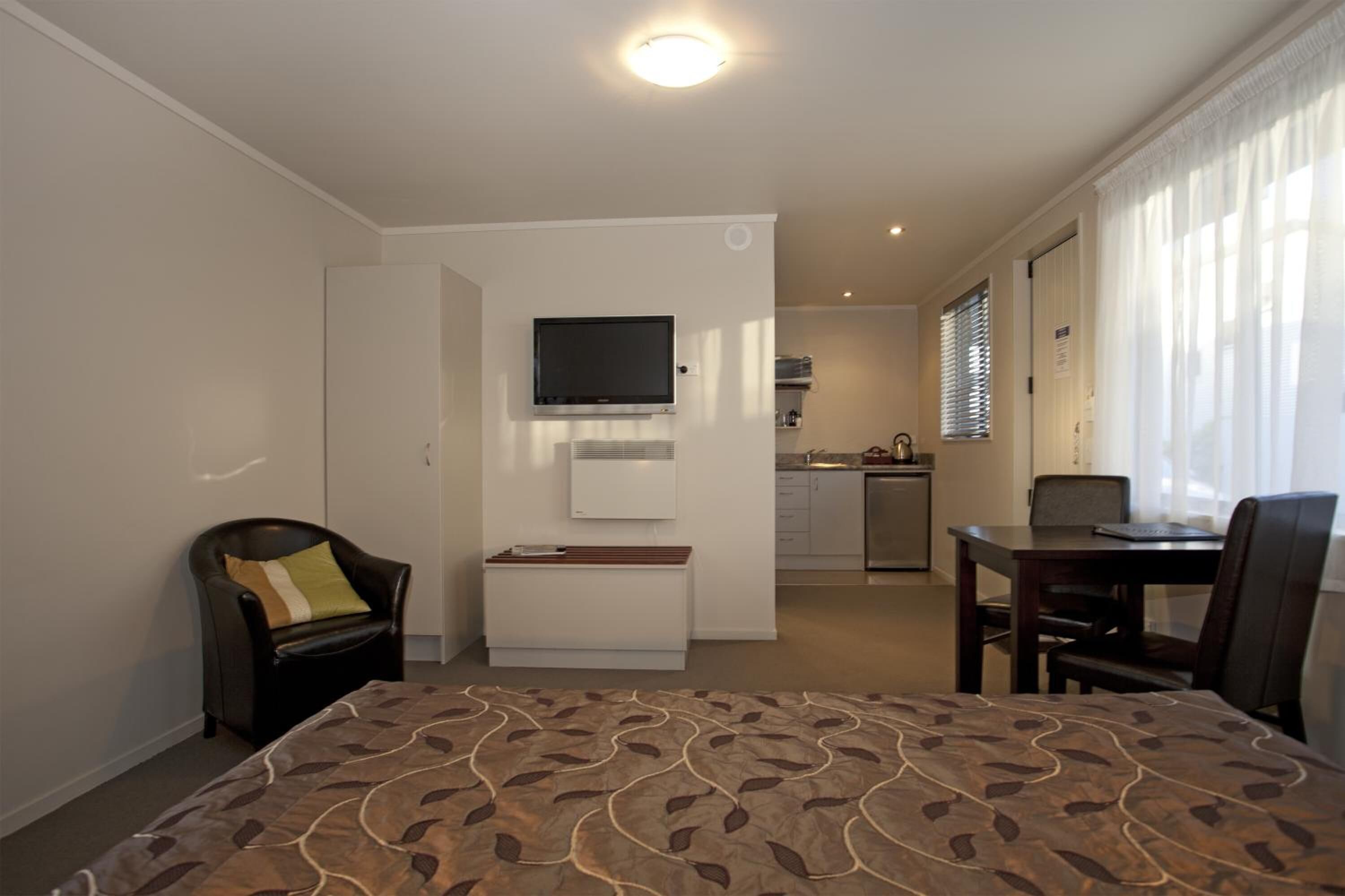 A hotel room with a bed, a desk, a chair, a television, a kitchenette, and a bathroom.