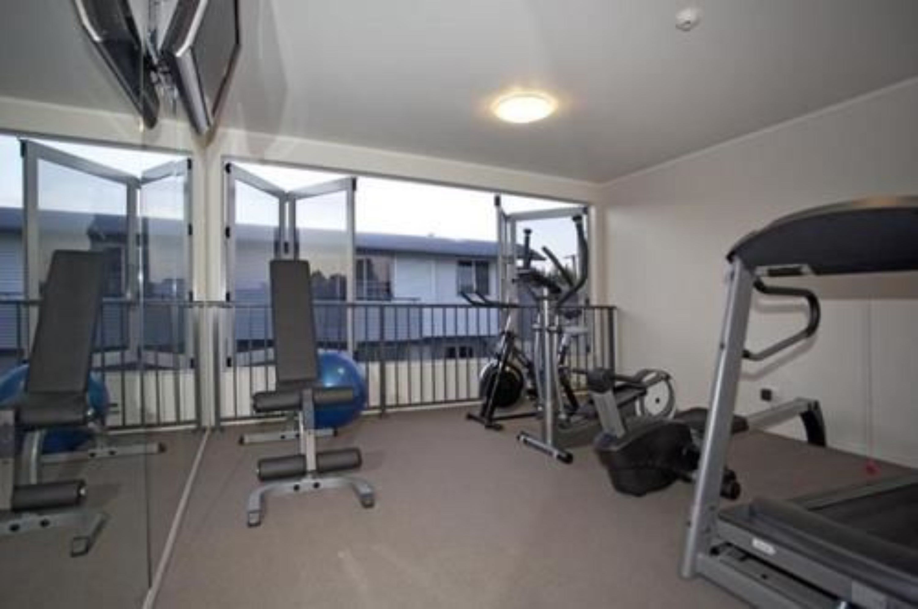 A gym with exercise equipment, a treadmill, and a large window offering a view of the city.