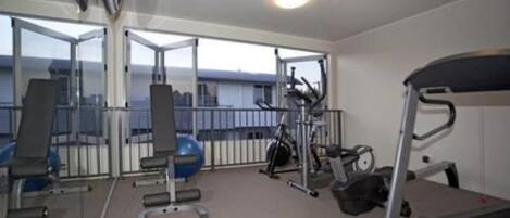 A gym with exercise equipment, a treadmill, and a large window offering a view of the city.