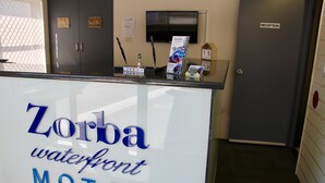 Un mostrador de recepción en el motel Zorba Waterfront, con un letrero, un televisor y un perchero.