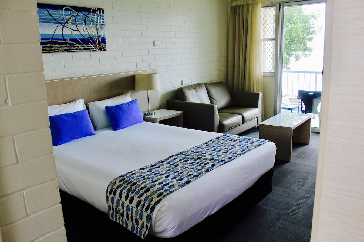 A hotel room with a bed, a sofa, a coffee table, and a view of the outdoors.