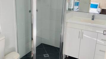 Une salle de bain moderne avec une douche à parois de verre, des toilettes blanches et un meuble-lavabo avec un miroir.