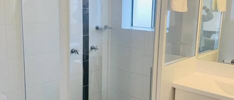 Ein Badezimmer mit einer Duschkabine, weißen Fliesen, einer weißen Toilette und einem weißen Waschbecken mit Spiegel darüber.