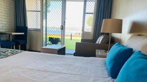 Habitación de hotel con una cama grande, un escritorio, una silla y vistas al exterior a través de un ventanal.