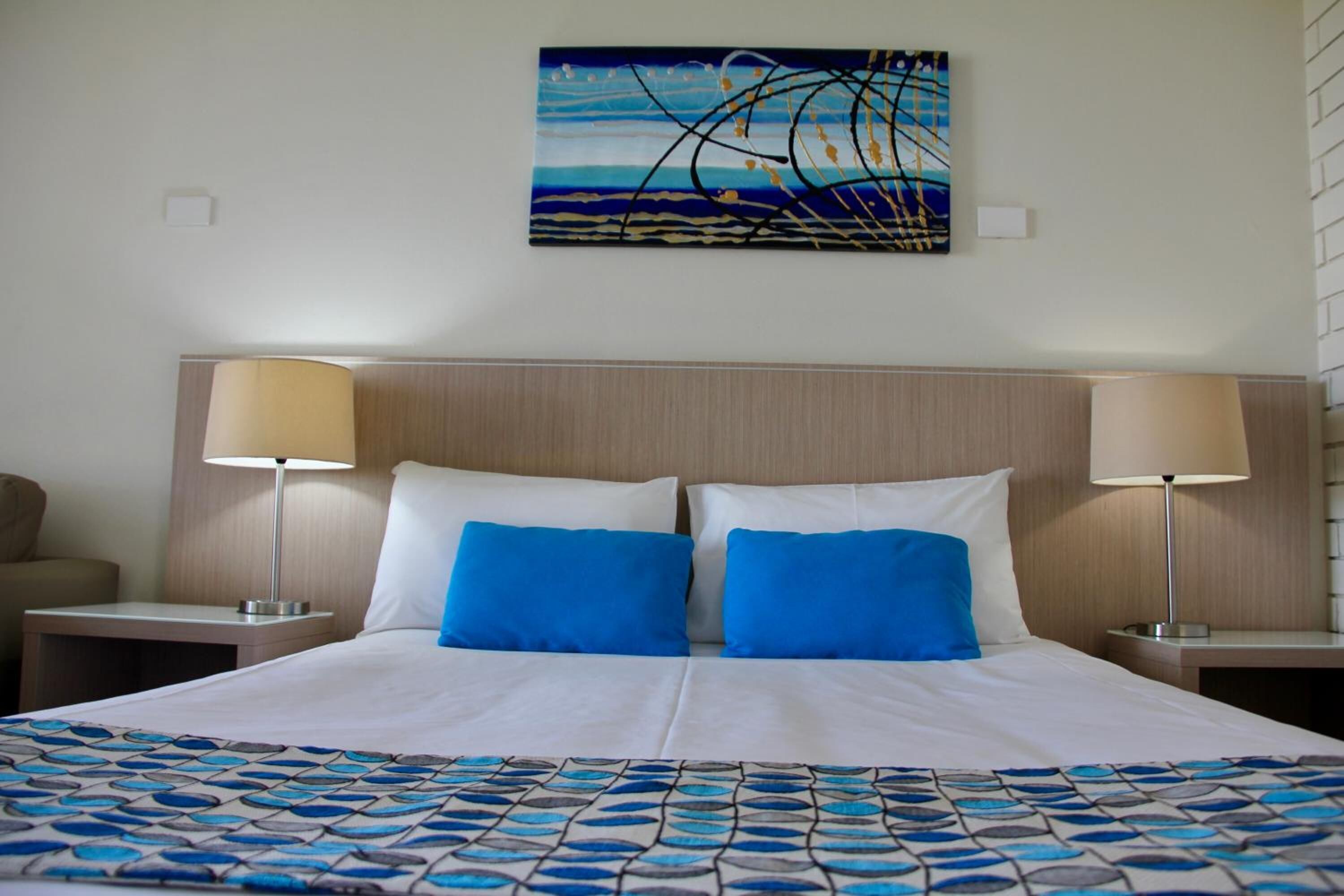 Een hotelkamer met een groot bed, twee nachtkastjes, een hoofdeinde en een schilderij aan de muur.