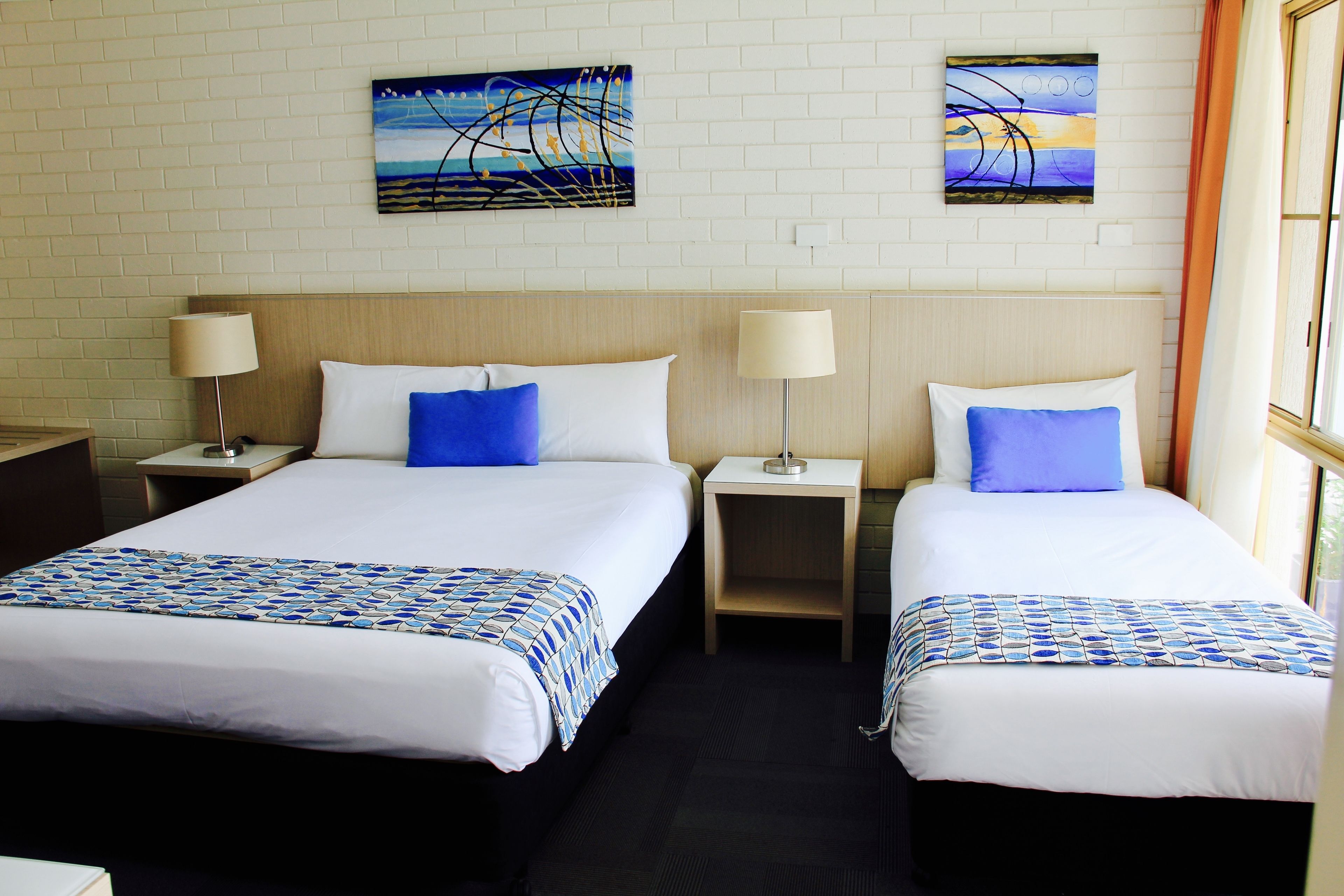Ein Hotelzimmer mit zwei Betten, jeweils mit einer blau-weißen Bettdecke, weißen Kissen und passenden Nachttischen mit Lampen.