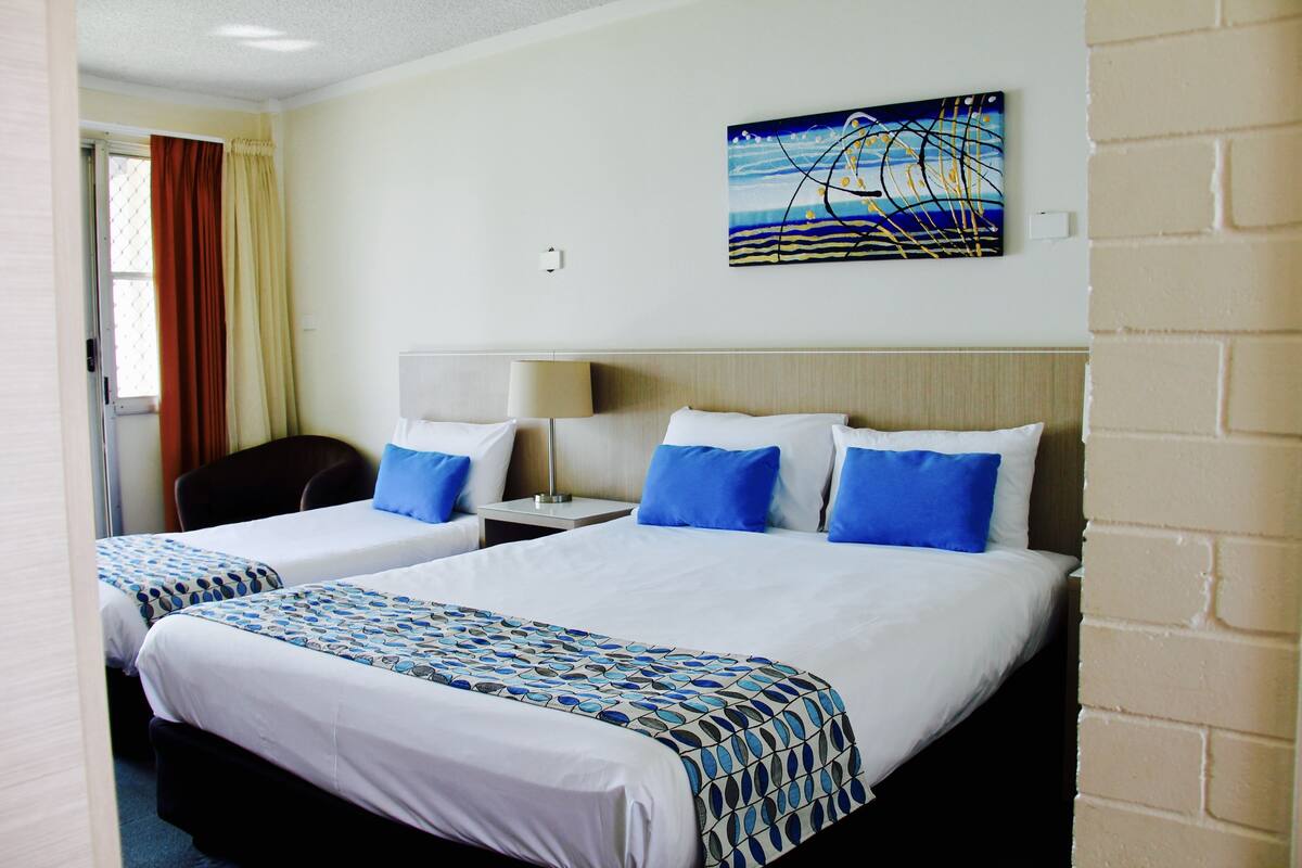 A hotel room with two beds, a desk, a chair, a lamp, and a painting on the wall.