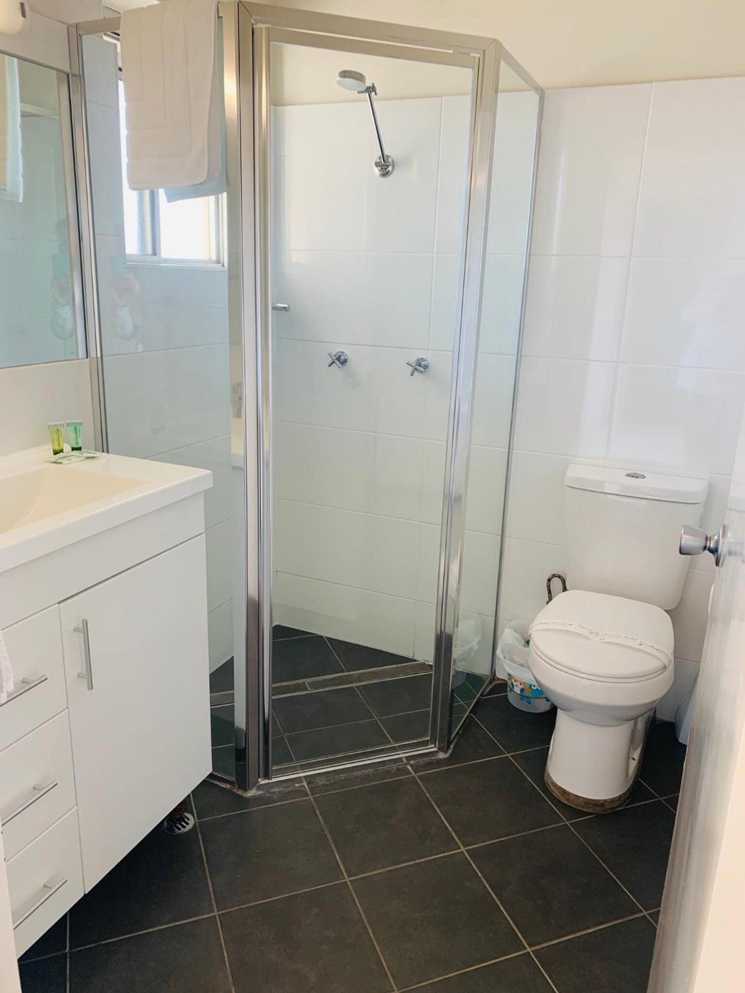 A modern bathroom with a glass-enclosed shower, white tiles, a white sink, and a toilet.