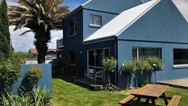A modern two-story house with a blue exterior, a front porch, and a wooden picnic table. - Phoenix Motel (Temuka)