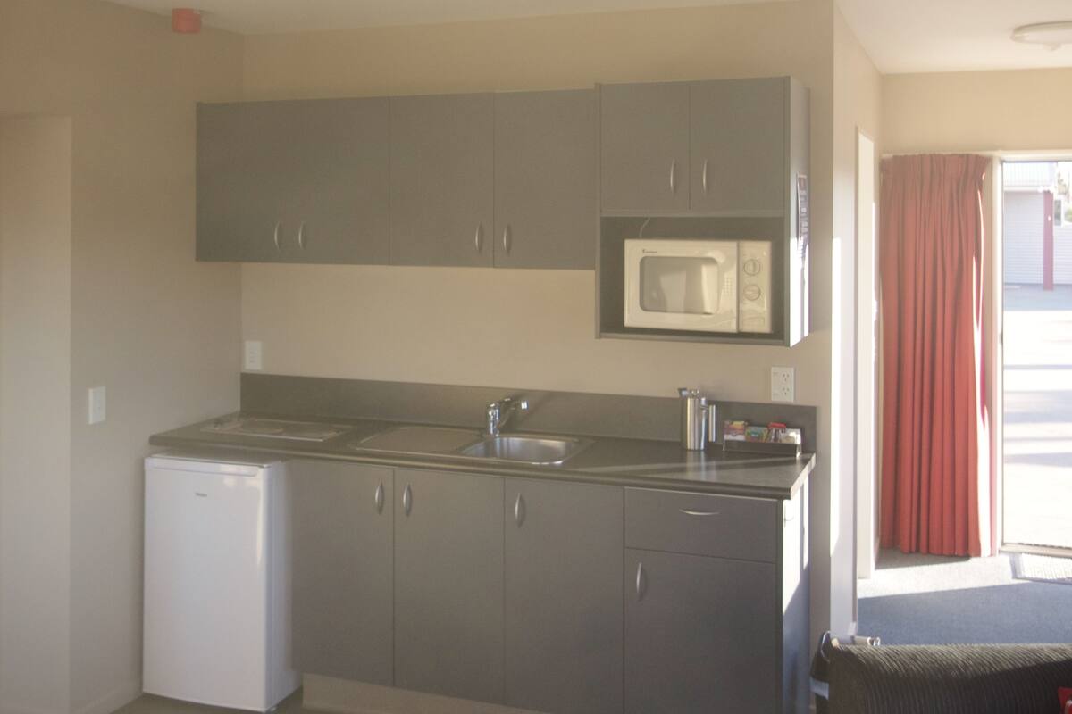 A compact kitchen with grey cabinets, a built-in microwave, and a small refrigerator.