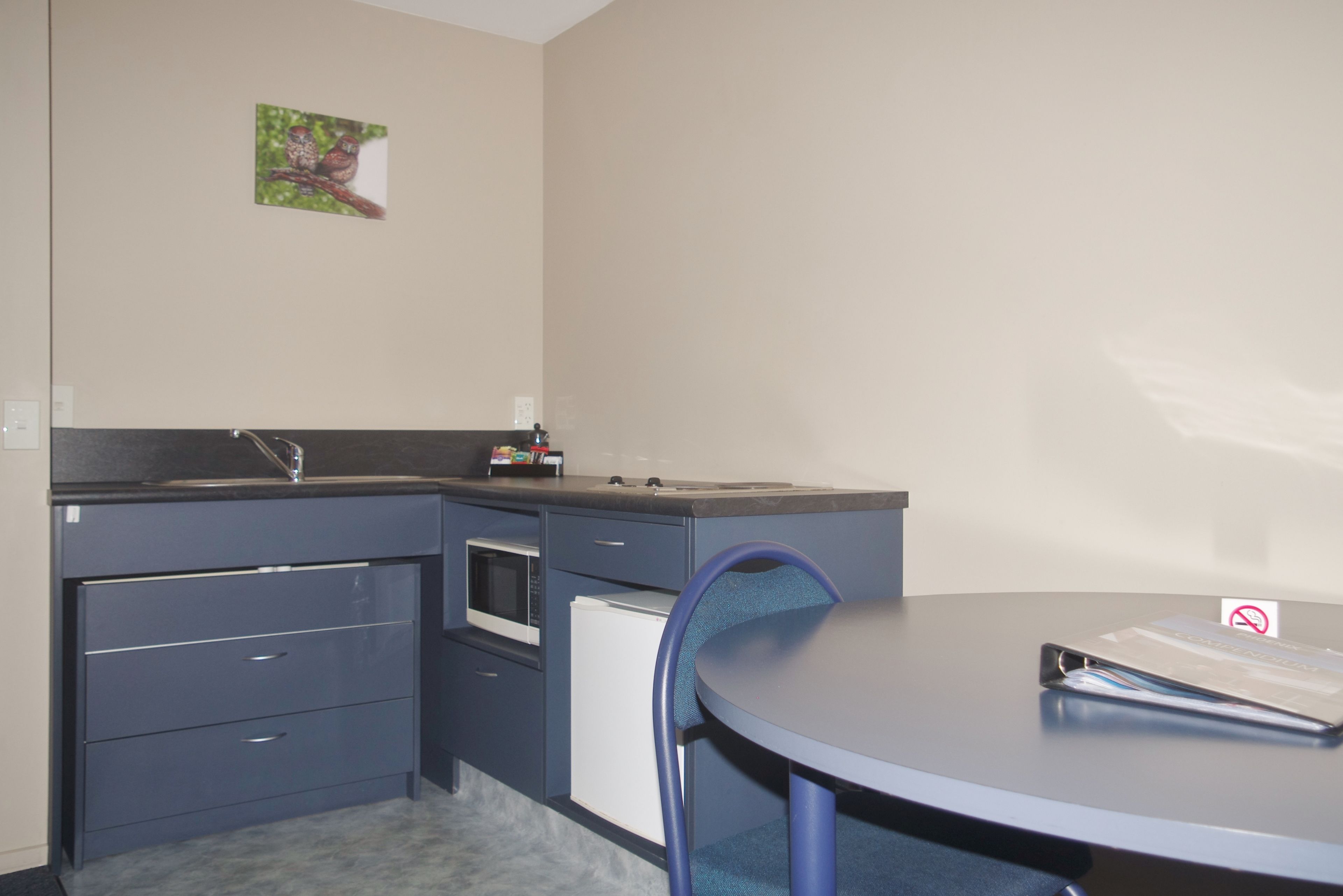A compact kitchen with a microwave, oven, and refrigerator. There is a small table and a chair.