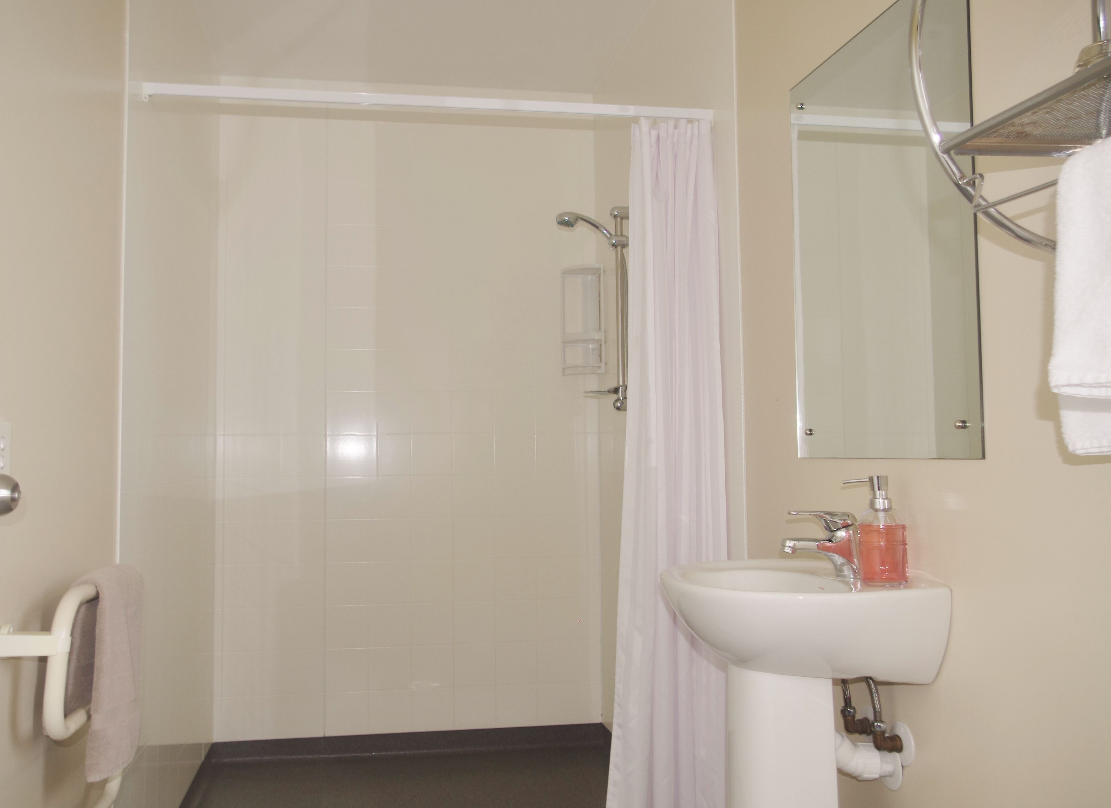 Un baño con ducha, lavamanos, espejo y toallero.