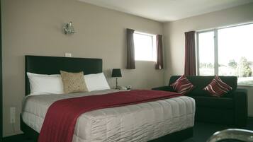 A hotel room with a bed, a sofa, a window with curtains, a wall-mounted light fixture, and a telephone.