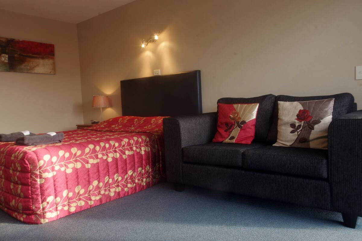 A bedroom with a bed, a sofa, a headboard, and a wall-mounted light fixture.