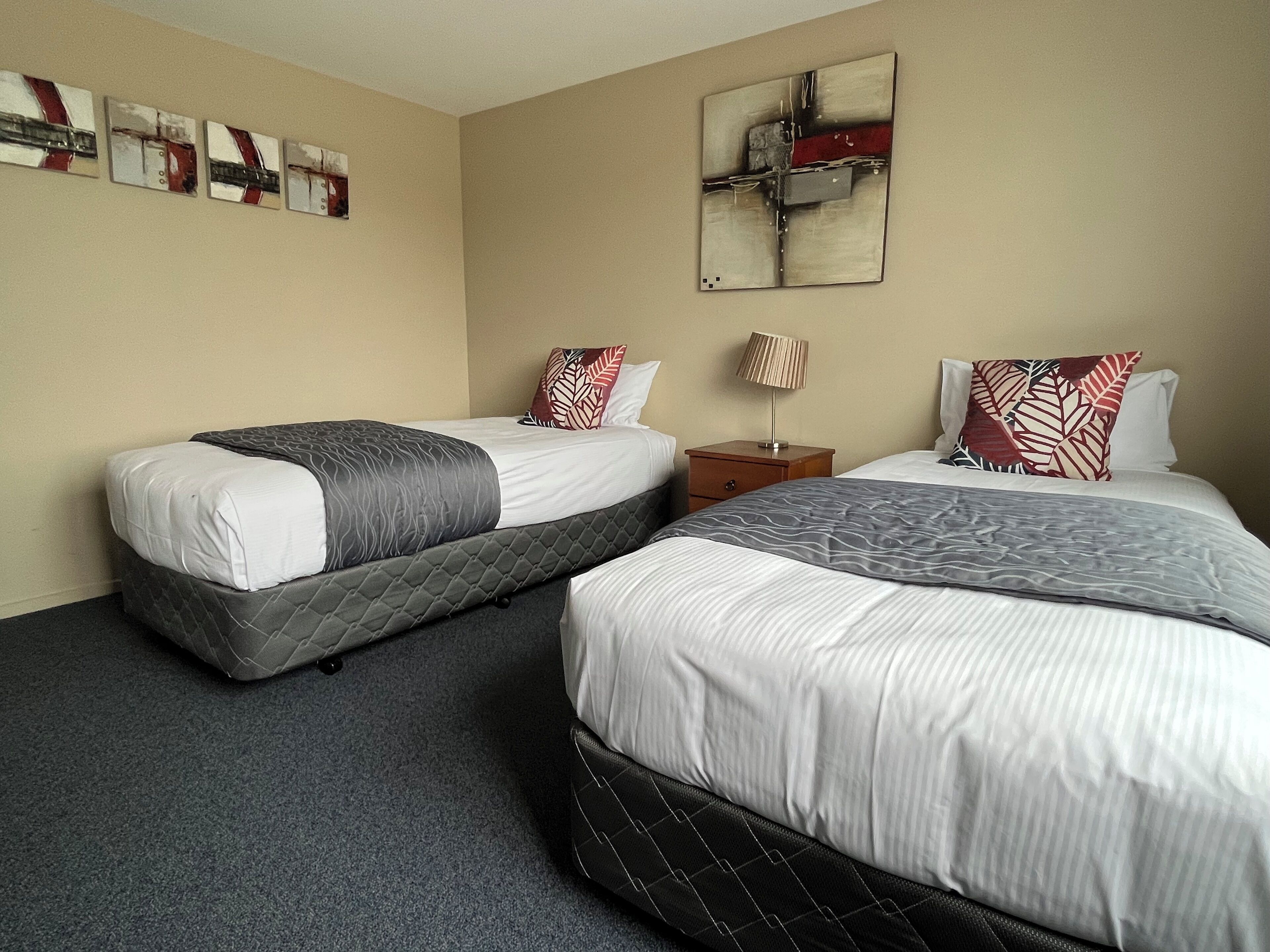 A hotel room with two beds, a nightstand, a lamp, and abstract wall art.