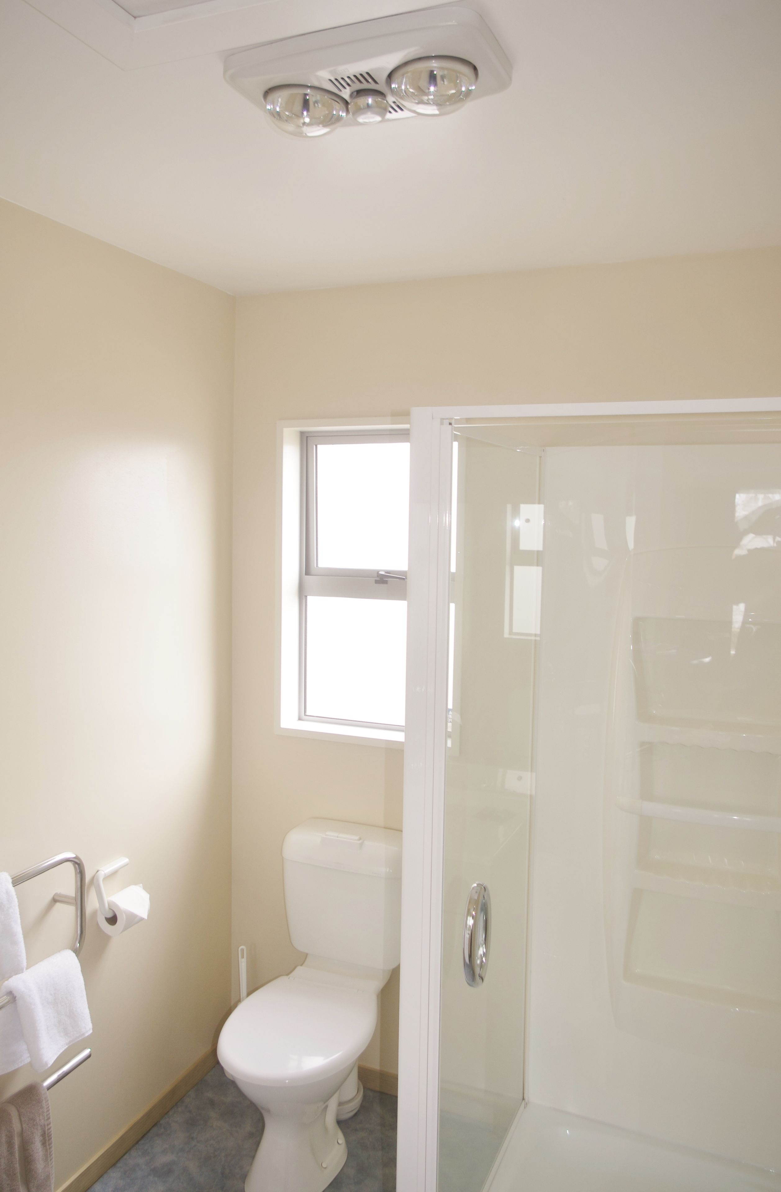 A bathroom with a toilet, a glass shower enclosure, a window, and a towel rack.