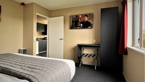 A hotel room with a bed, a desk, a chair, a mirror, and a window with a red curtain. - Phoenix Motel (Temuka)