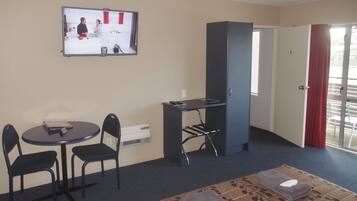 Une petite pièce avec un coin cuisine, une table avec des chaises, un téléviseur et une porte donnant sur un balcon.
