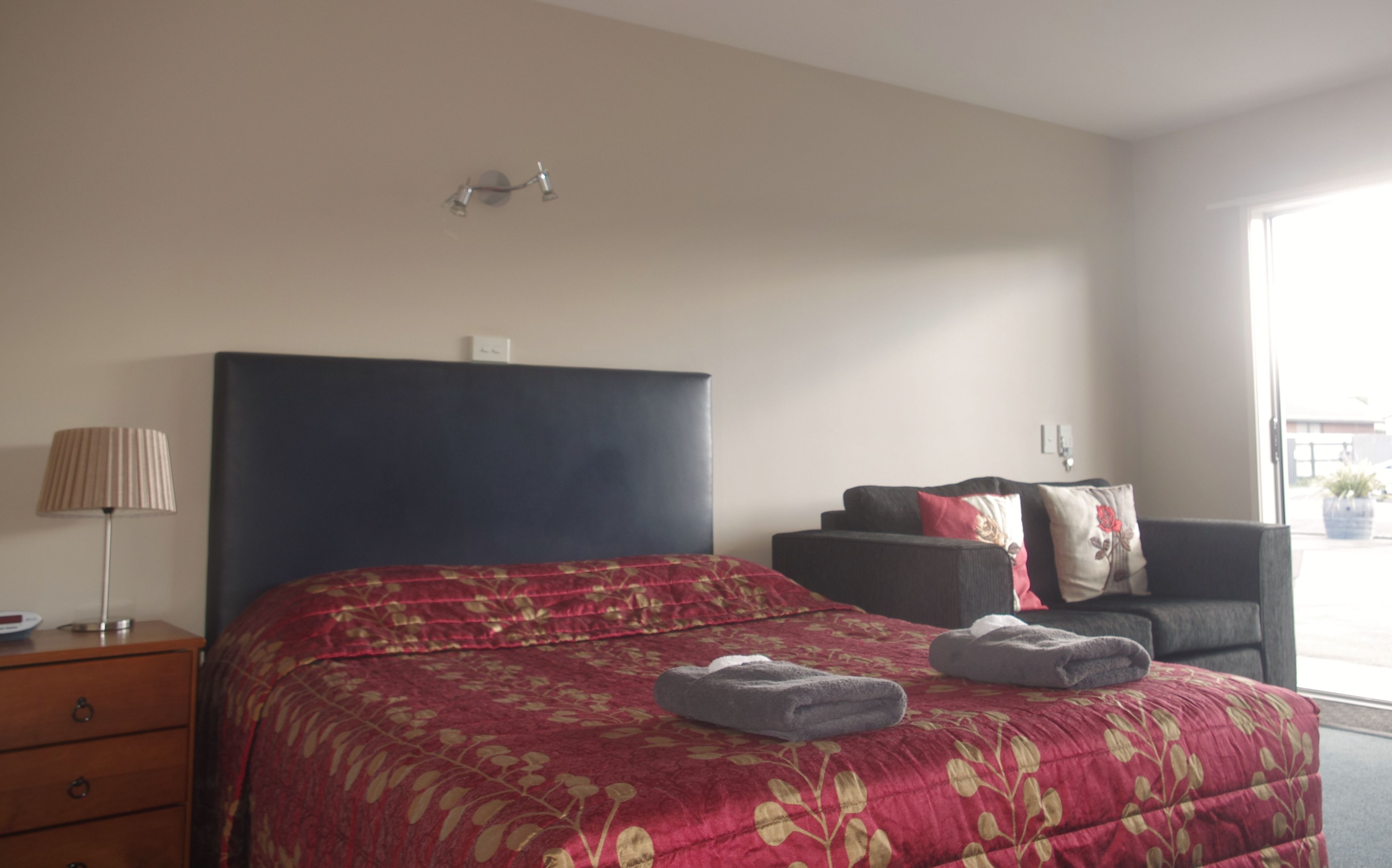 Une chambre d’hôtel avec un lit, une table de chevet, une lampe, un canapé et une fenêtre.