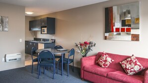 A compact living space with a kitchenette, dining area, and a red sofa with floral cushions. - Phoenix Motel (Temuka)